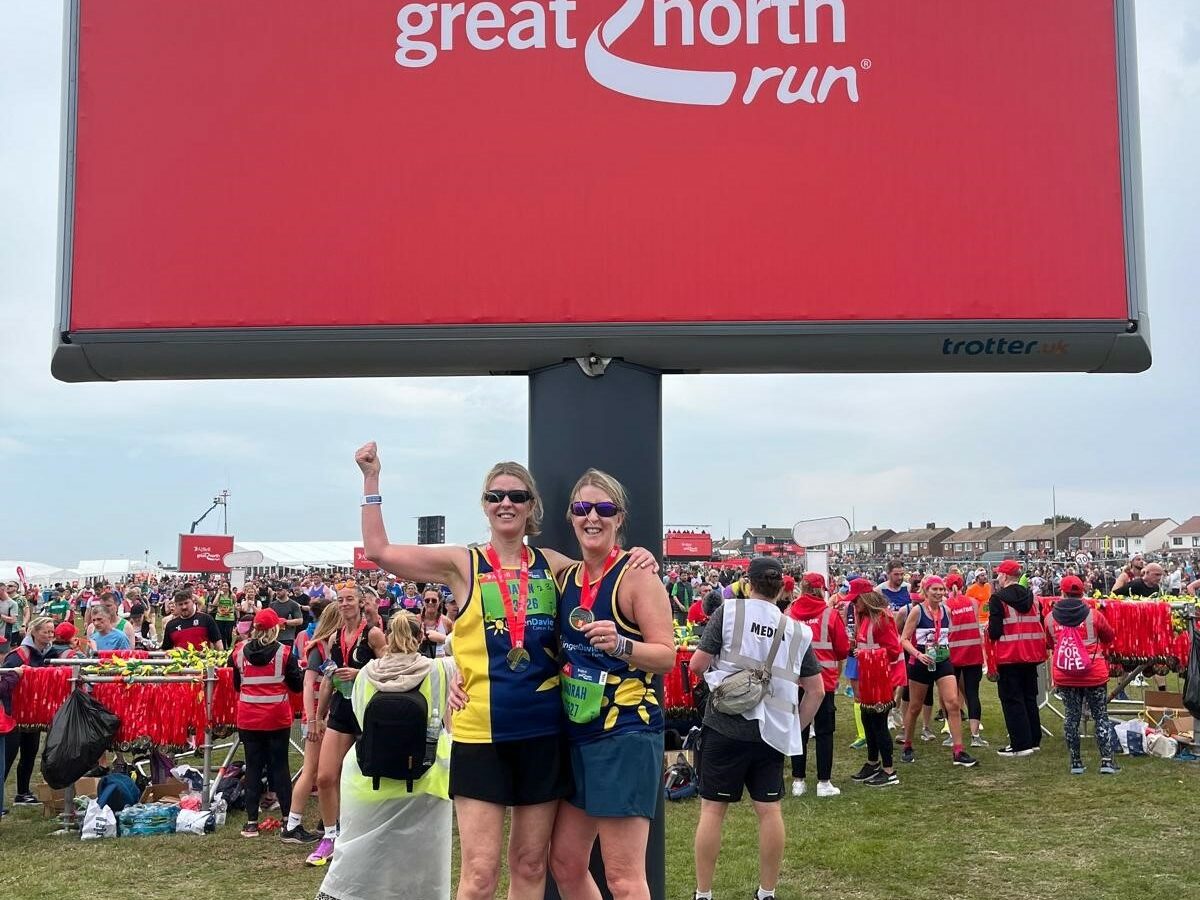 Two female runners stood with their medals underneath the Great North Run sign