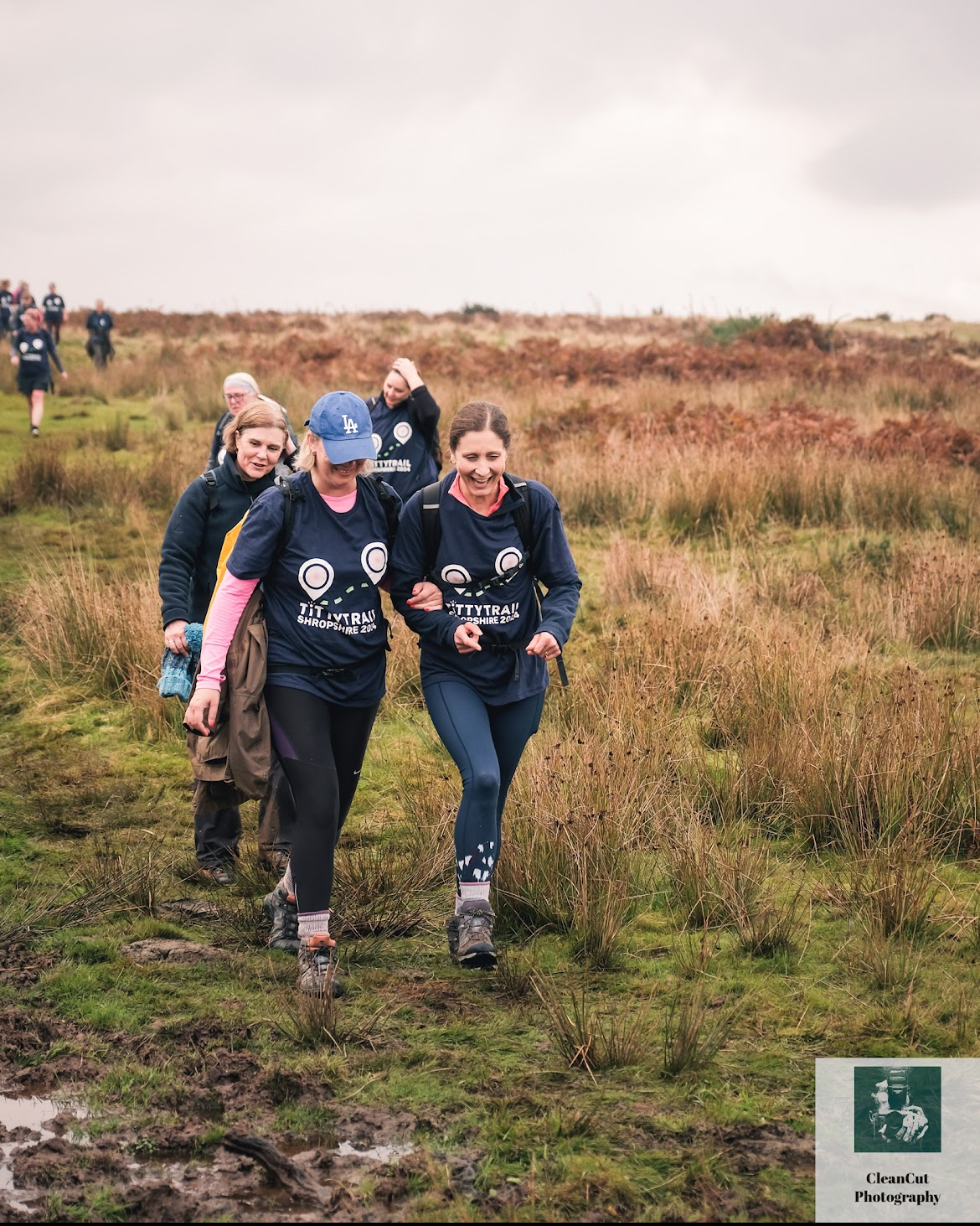 A group of women in matching navy tops walking arm in arm across the top of a hill