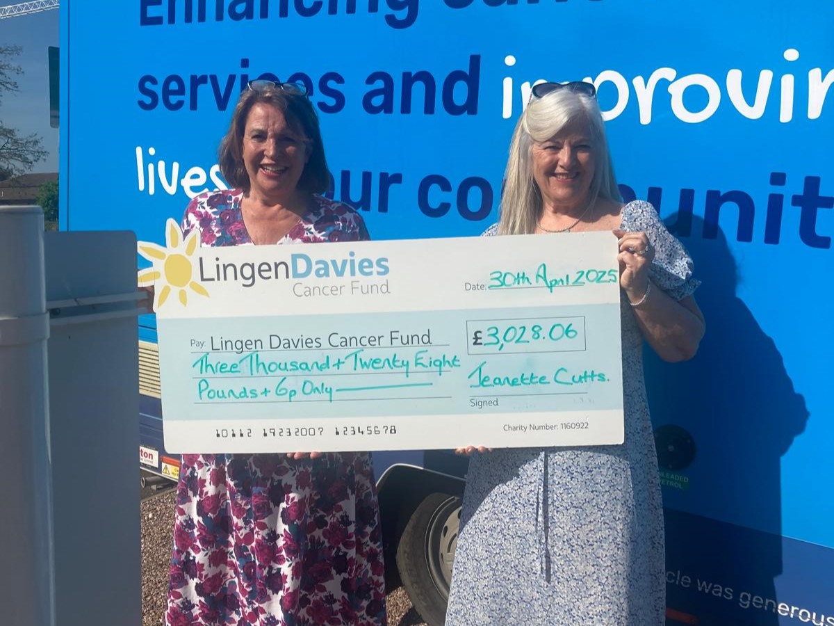 Two women stood in front of a blue background. They are holding a giant cheque which reads, 'Lingen Davies Cancer Fund, Three Thousand + Twenty Eight Pounds'.