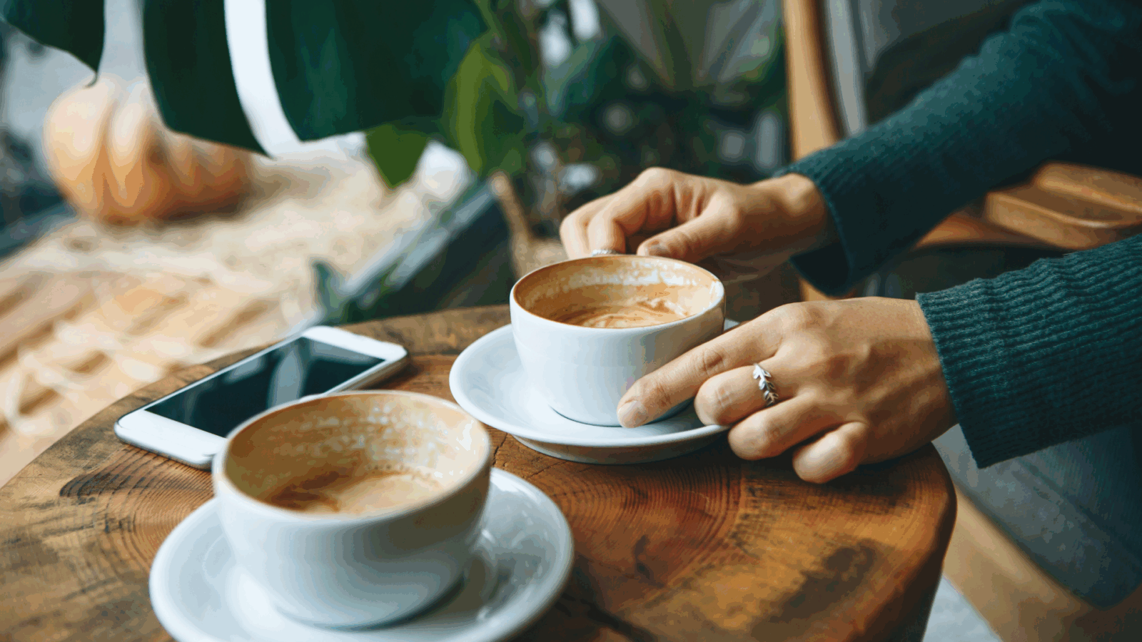 Two coffee cups sat on a coffee table with a hands picking one of the cups up.