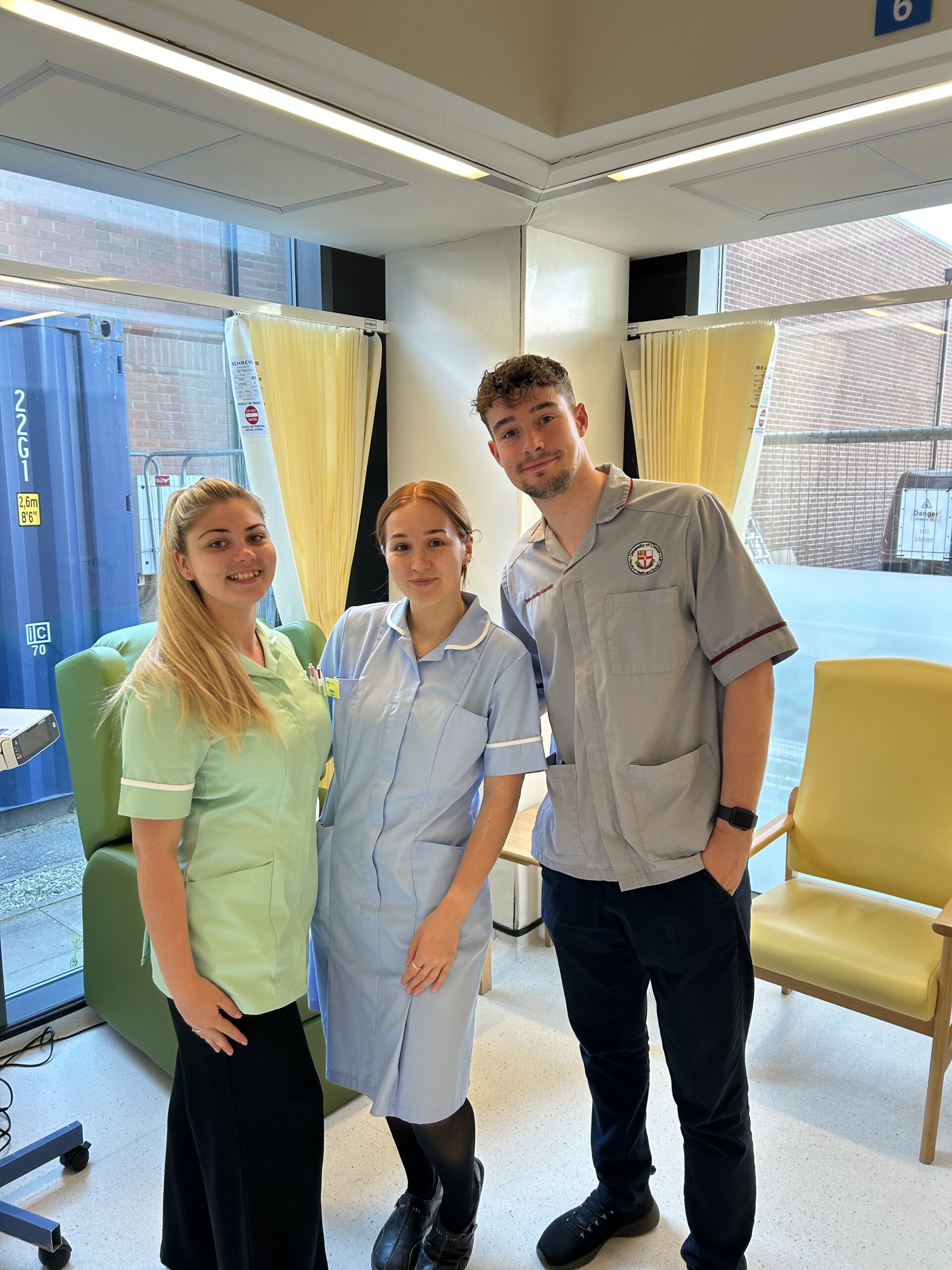 Three medical staff posing for a photo in front of a chemotherapy treatment bay.